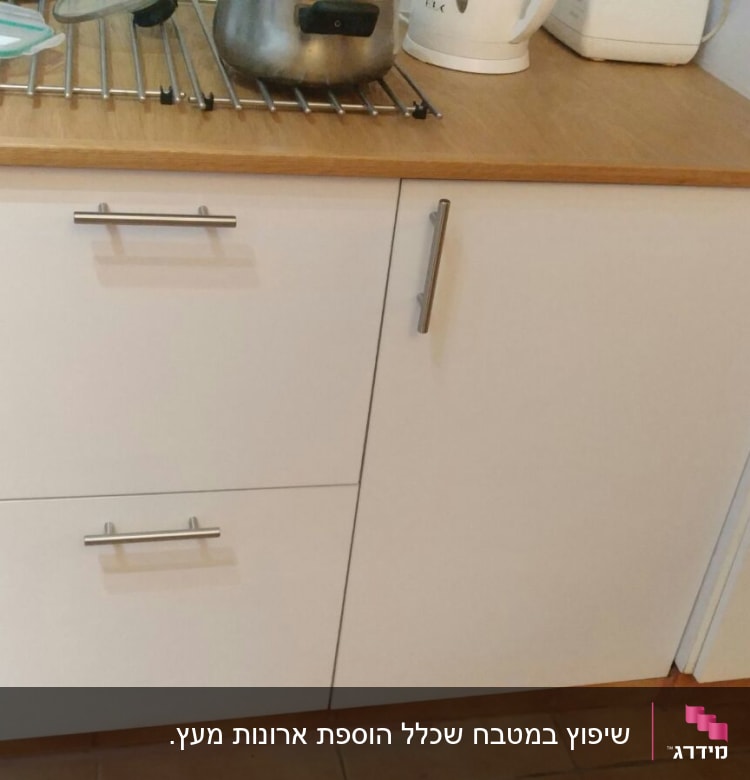 ארונות מטבח לבנים עם ידיות מתכת, קומקום וסיר על משטח עץ